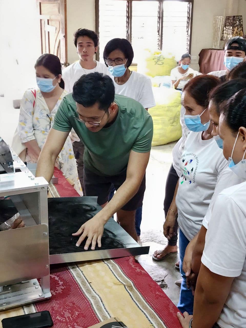 Capilli staff and students gathered around a hair felting machine — learning how hair waste is transformed into eco-friendly products